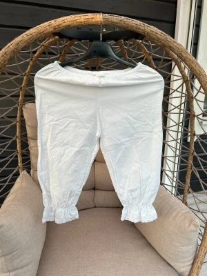 Mameluki - Säljer ett par vita byxor med resår i midjan och volangdetaljer vid bensluten. Byxorna har en avslappnad passform och är perfekta för en bekväm och stilren look. Passar perfekt att ha under klänning