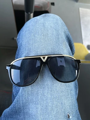 Svarta  solglasögon - Snygga svarta solglasögon med silvriga detaljer och mörka glas. Klassisk pilotformad båge med en tydlig V-detalj framtill och logotyp på sidan. Perfekta för dig som vill ha en exklusiv och trendig look.