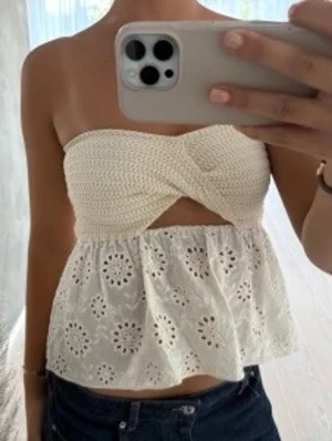 Vit virkad bandeau topp Zara - Supersöt vit bandeau topp med virkad överdel och broderad, utsvängd nederdel med hålmönster. Toppen är axelbandslös och har en twistad detalj framtill. 