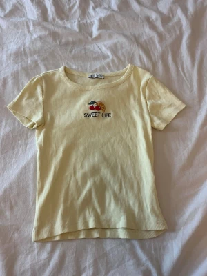 Gul ribbad t-shirt med brodyr - Söt ljusgul ribbad t-shirt med korta ärmar.