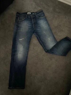 Archieve mörkblåa jeans med slitningar - Snygga mörkblå jeans med raka ben och små slitningar på framsidan vilket speglar en trendig design. Perfekt för dig som vill ha ett par trendiga jeans till hösten