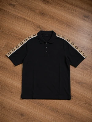 Gucci pikétröja svart - Svart pikétröja i Gucci med krage och knappar framtill. På axlarna och ärmarna finns beige band med logomönster som ger en cool kontrast. Kortärmad och i klassisk passform, perfekt till jeans eller shorts.