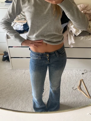 Blå bootcut jeans med låg midja - Säljer ett par blå bootcut jeans med låg midja och klassiska fickor både fram och bak. Jeansen har en snygg tvätt och lätt utsvängda ben. Perfekta för dig som gillar  och avslappnad stil. Materialet är denim i bomull.