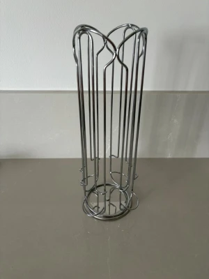 Metallställ för kapslar, dulce gusto - Säljer ett cylinderformat ställ i silverfärgad metall, perfekt för att förvara kaffekapslar från dulce gusto. Stället är roterbart och har en öppen design med flera fack och rundad topp. Passar bra på köksbänken för enkel åtkomst.