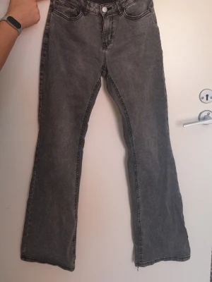 Gråa bootcut jeans med rå kant - Säljer ett par gråa bootcut jeans med regular midja och råa, avklippta benslut. Jeansen har klassiska fem fickor och synliga sömmar. Perfekta för en avslappnad och trendig look.