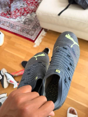 Puma svarta fotbollsskor med neon - Säljer ett par svarta fotbollsskor från Puma med neonfärgade detaljer och logga. Skorna har snörning, mönstrad ovandel och sulor med gula dobbar för bra grepp på planen. Perfekta för dig som vill sticka ut på matchen!