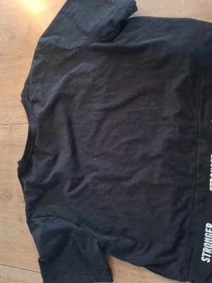 Svart t-shirt från Stronger - En svart t-shirt från Stronger med klassisk passform och rund hals. Tillverkad i mjukt bomullsmaterial och har korta ärmar. Perfekt för en avslappnad och sportig stil.