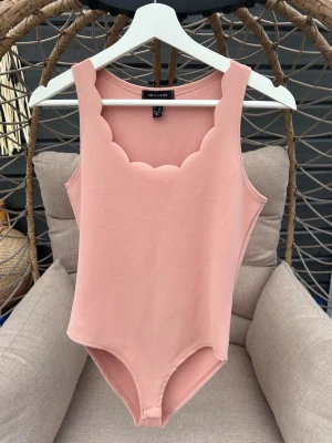 Rosa scallop body från New Look - Supersnygg rosa body från New Look med scallop-detaljer vid urringningen. Ärmlös modell i mjukt stretchigt material som sitter skönt på kroppen. Perfekt att styla till jeans eller kjol för en trendig look.