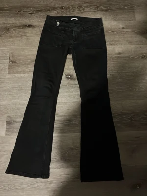 Svarta bootcut jeans med detaljer - Snygga svarta bootcut jeans med utsvängda ben och dekorativa detaljer på bakfickorna. Jeansen har låg midja och klassisk femficksdesign. Materialet ser ut att vara stretchigt för extra komfort. Perfekta för dig som gillar en retroinspirerad look.