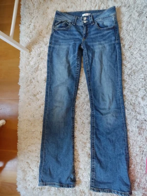 Blå bootcut jeans med dubbla knappar - Ett par klassiska blå bootcut jeans med dubbla knappar i midjan från Gina Tricot. Jeansen har en lätt tvättad look och utsvängda ben.