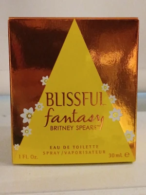 Blissful Fantasy Britney Spears parfym - Blissful Fantasy från Britney Spears är en Eau de Toilette i en rund flaska med gul och orange färgton. Förpackningen har en glansig orange yta med gula detaljer och blommotiv. Innehåller 30 ml spray. Ny men testad 1 sprut.