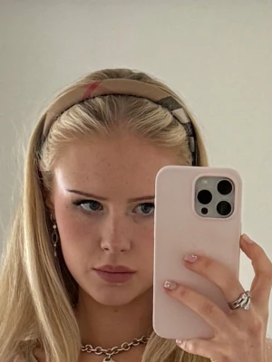 Burberry rutigt diadem i beige - Autentiskt diadem från Burberry i klassiskt beige rutigt mönster med inslag av svart, vitt och rött. Diademet har en mjuk, vadderad form och är klätt i tyg med Burberrys ikoniska design 🫶🏻🫶🏻🌷