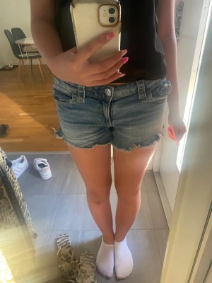 Blå jeansshorts med fransig kant - Säljer ett par klassiska blå jeansshorts med fransig kant. Shortsen har normal passform och stängs med knapp och dragkedja. Perfekta för varma dagar och enkla att matcha med olika toppar.