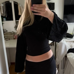Svart croppad långärmad topp - Säljer en svart croppad topp med långa, vida ärmar och hög hals. Toppen har en clean och stilren look som passar perfekt till både jeans och kjol. Materialet känns mjukt och följsamt mot kroppen. Aldrig använd!