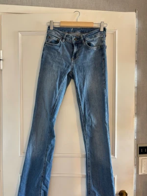Ljusblå bootcut jeans - Säljer ett par ljusblå bootcut jeans med klassisk femficksdesign och medelhög midja. Jeansen har en snygg tvätt och är tillverkade i ett mjukt denimtyg som är stretchig. midjemåttet tvärs över är ca 32cm. vet inte storleken då jag klippt av lappen men skulle tippa på 24/25