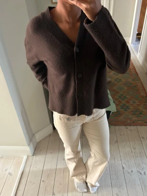 Mörkbrun kofta med knappar - Mysig mörkbrun kofta med v-ringning och fyra stora knappar framtill. Koftan har långa ärmar och ribbade muddar vid ärmslut och nederkant. Passar perfekt till jeans eller kjol för en avslappnad look.
