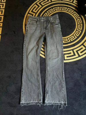 Grå flared jeans från Zara  - Säljer ett par grå raka jeans från ZARA med råa, fransiga benslut. Jeansen har klassisk femficksdesign och är tillverkade i denim. Perfekta för en avslappnad och trendig look.