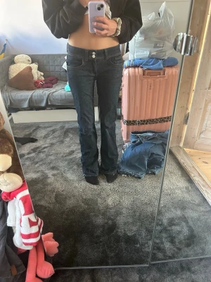 bootcut jeans - Säljer ett par mörkblå bootcut jeans med klassisk femficksdesign och låg midja. Jeansen har en snygg tvätt och raka ben som går ut lite nedtill. Perfekta till sneakers eller boots för en avslappnad look.