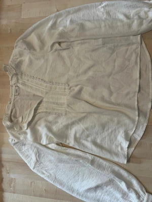 Vit blus med spetsdetaljer från JDY - Söt vit blus från JDY med långa ärmar och fina spetsdetaljer längs v-ringningen. Blusen har en liten volang vid halsen och ett mjukt, tunt tyg som ger en avslappnad känsla. Perfekt att styla med jeans eller kjol för en trendig look. Tar bud!