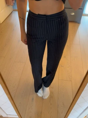 Svarta kostymbyxor med vita ränder - Snygga svarta kostymbyxor med vita smala kritstrecksränder och raka ben. Byxorna har hög midja och klassisk stängning framtill. Perfekta för en stilren och trendig look.