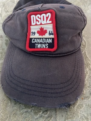 Mörkblå DSQ2 keps med patch - Snygg mörkblå keps från DSQ2 med broderad patch framtill där det står 'Canadian Twins' och en röd lönnlöv. Kepsen har böjd skärm och ventilationshål i kontrasterande färg. Justerbar baktill för perfekt passform. Materialet är slitstark bomull.