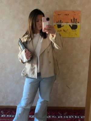 Beige trenchcoat med bälte - Stilren beige trenchcoat med knytskärp i midjan och bred krage. Jackan har dubbelknäppning framtill och är tillverkad i ett mjukt material som ger en avslappnad men ändå chic look. Perfekt för lager-på-lager och passar till jeans eller klänning.