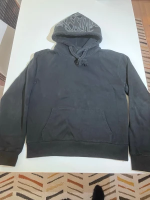 Syna world hoodie - Svart hoodie från Syna world med tryck i vitt på huvan. Köpt för 230£ och är fortfarande i topp skick! Fläckarna på bilden går att tvätta bort, har bara inte använt den på länge.