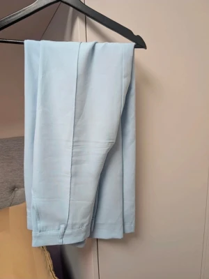 Ljusblå kostymbyxor från Madlady - Snygga ljusblå straight leg kostymbyxor från Madlady med pressveck och raka ben. Byxorna har en klassisk passform med mycker stretch. Uppsydda för att passa en på 165 cm. Som ny