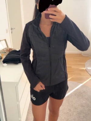 Svart lättviktsjacka med dragkedja - Säljer en svart lättviktsjacka med dragkedja framtill och hög krage. Jackan har en clean look och är perfekt för lager-på-lager. Tillverkad i syntetmaterial och har lång ärm. Passar dig som gillar en enkel och sportig stil.