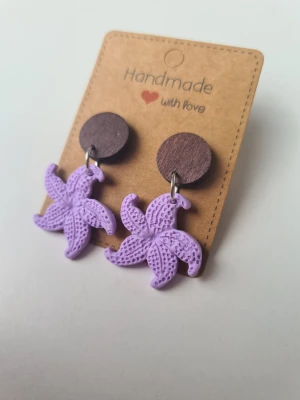 Lila handgjorda sjöstjärneörhängen  - Unika handgjorda örhängen med hängande sjöstjärnor i lila polymerlera. Örhängena har en lekfull och trendig design och är lätta att bära. Gjorda för hand av mig i polymerlera. 