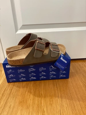 Birkenstock Arizona  - Snygga oliv gröna Birkenstock sandaler med två breda remmar och justerbara metallspännen. Klassisk och bekväm design som passar till många stilar.