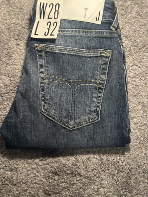 Blå tiger of Sweden jeans slim fit jeans W28 L32 - Snygga blå slim fit jeans med klassisk femficksmodell och kontrastsömmar. Jeansen har en lätt tvättad look och smal passform som sitter tajt längs benen. Perfekta för en trendig och avslappnad stil.