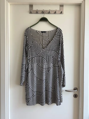 Svartvit prickig klänning Vero Moda - Säljer en svartvit klänning från Vero Moda med coolt prickigt mönster i cirklar. Klänningen har lång ärm och är i kort modell. Perfekt för dig som gillar grafiska prints och vill sticka ut lite extra.