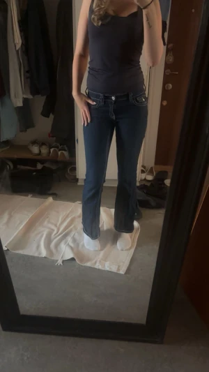 Jeans  - Säljer ett par mörkblå bootcut jeans med vita kontrastsömmar och snygga fickdetaljer bak. Jeansen har normal passform och är tillverkade i bomull. Perfekta för dig som gillar klassisk denimstil med lite extra edge.