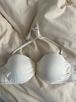 Vit bandeau bikiniöverdel - Snygg vit bandeau bikiniöverdel med avtagbara axelband och gulddetalj i mitten. Storlek 80C 
