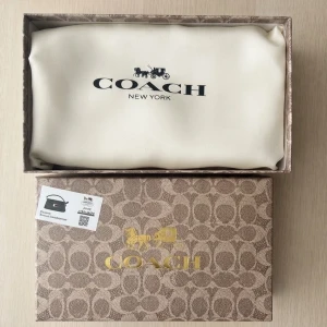 Svart handväska från Coach - Snygg svart handväska från Coach i äkta läder med guldfärgat C-spänne framtill. Väskan har en stilren och klassisk design med lock och struktur i materialet. Levereras med originalbox och dustbag.  Priset kan diskuteras 