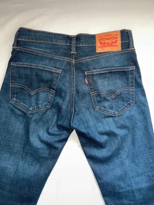 Mörkblå Levi's jeans med raka ben - Snygga mörkblå jeans från Levi's med klassisk femficksmodell och raka ben. Jeansen har kontrastsömmar, läderpatch bak i midjan och den ikoniska röda Levi's-taggen på bakfickan. Tillverkade i slitstark denim som passar perfekt till din vardagsstil.