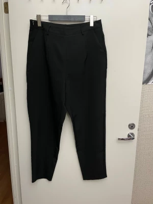 Svarta chinos dam, stl 42  - Snygga svarta chinos byxor med hög midja. Byxorna har bälteshällor, sidofickor och dragkedja i sidan för en clean look. Perfekta till en dressad outfit och passar till många olika stilar. Stl 42