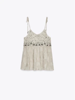 Beige broderad topp med tunna band - Oanvänd från Zara köpt förra sommaren, nypris 700. Söt beige topp med tunna axelband som knyts. Toppen har broderade blommor i svart och silver över bysten och ett lätt, flowy tyg med subtilt mönster. Perfekt för en avslappnad och trendig look.