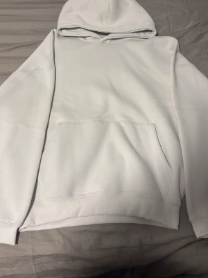 Vit/grå basic oversized hoodie med huva - Säljer en enkel och stilren vit hoodie med huva och stor magficka. Hoodien har ribbade muddar vid ärmslut och nederkant. Perfekt för dig som gillar en clean och avslappnad look. Materialet känns mjukt och bekvämt.