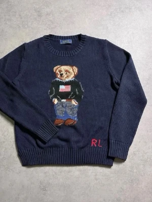 Mörkblå stickad tröja från Ralph Lauren  - Priset kan diskuteras, Mörkblå stickad tröja från Polo Ralph Lauren med ikoniska Polo Bear-motivet framtill. Rund halsringning, ribbade muddar och RL-broderi nertill. Hundra procent riktigt med Ralph lauren påsen! Perfekt för dig som gillar klassisk preppy stil och vill ha något som sticker ut. Detta är ett måste!  