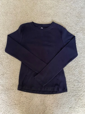 Mörkblå långärmad tröja - En enkel och stilren mörkblå långärmad tröja i ribbat material. Tröjan har rund halsringning och smal passform, perfekt att bära som basplagg eller under en hoodie. 