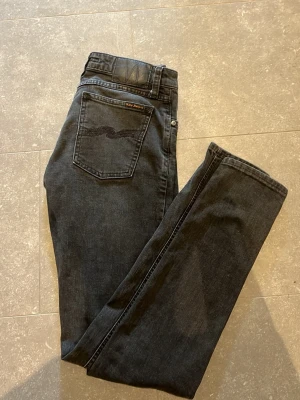 Nudie jeans bra skick - Storleken är W29 L32 .Snygga svarta jeans från Nudie Jeans med ett riktigt bra skick. Jeansen har en diskret logga på bakfickan och är tillverkade i ett mjukt denimtyg. Perfekta för en avslappnad och stilren look.
