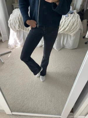 Svarta bootcut jeans - Säljer ett par svarta bootcut jeans med låg midja och klassisk femficksdesign. Jeansen har en snygg utsvängd passform nedtill och är perfekta för en trendig vardagslook. Materialet är denim med lite stretch för extra komfort. Uppspeätta nedtill för exktra längd