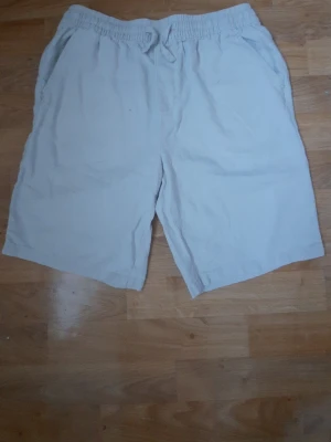 Linne shorts med snörning - Lätta och bekväma beiga shorts med elastisk midja och snörning. Shortsen har sidofickor fram och en bakficka. Perfekta för varma dagar och enkel stil Storlek 170! 
