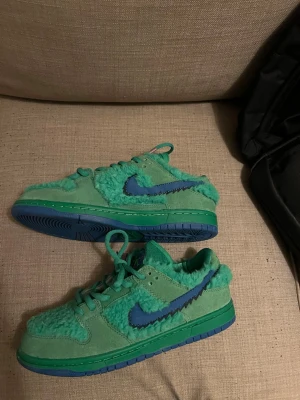 Nike SB dunk the grateful dead  - Unika gröna Nike Dunk Low sneakers med blå sula och blå swoosh. Skorna har en kombination av mocka och fluffigt tyg som ger en cool och lekfull look. Perfekta för dig som vill sticka ut med färg och stil. 