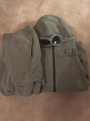 CP Company Set - Säljes cp company set, Storlek 14 i båda. Säljes båda tillsammans för 699kr.  De är i bra skick. Nypris över 3000kr hör av er vid frågor eller funderingar. Byxorna ingår lins saknas samt googles 
