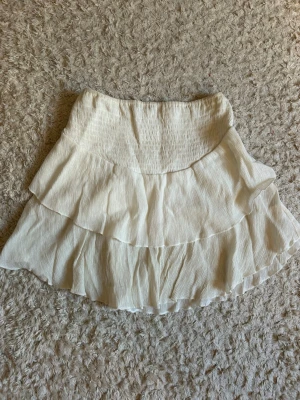 Vit volangkjol - Supersöt vit kjol med dubbla volanger. Kjolen är kort och har en luftig, flowy passform som passar perfekt till varma dagar. Tillverkad i ett tunt, skönt material som ger en avslappnad vibe. Stretchigt material🤗