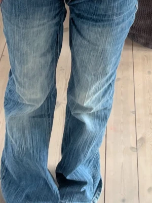 Blå utsvängda jeans med slitningar - Säljer ett par blå jeans med utsvängda ben och tydliga slitningar framtill. Jeansen har en klassisk femficksmodell och är tillverkade i denim. Perfekta för dig som gillar en retro och avslappnad stil. Vintage man får inte med skärpet!! Skulle säga att de e storlek xs/s jsg är 164 o de e lite långa