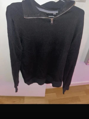 Svart halvzip  - En svart långärmad tröja med halvzip och hög krage. Tröjan har en enkel och stilren design med ribbade muddar vid ärmslut och nederkant. Perfekt för lager-på-lager och passar till många olika stilar.